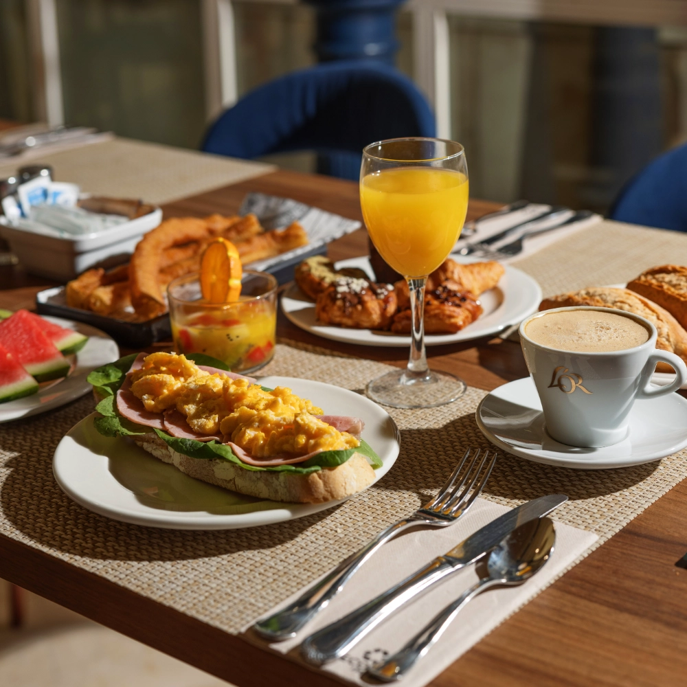 Desayuno con jugo, caf&eacute;, pan y frutas sobre la mesa.