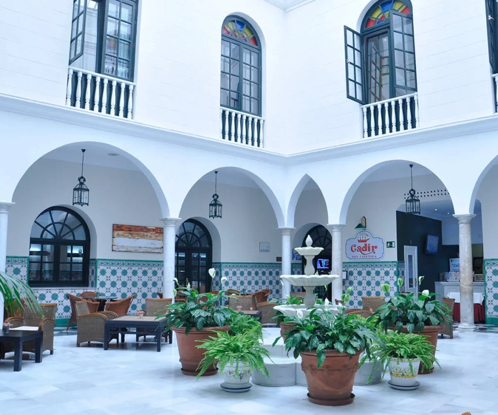 Patio interior blanco con arcos, fuentes y plantas en macetas.