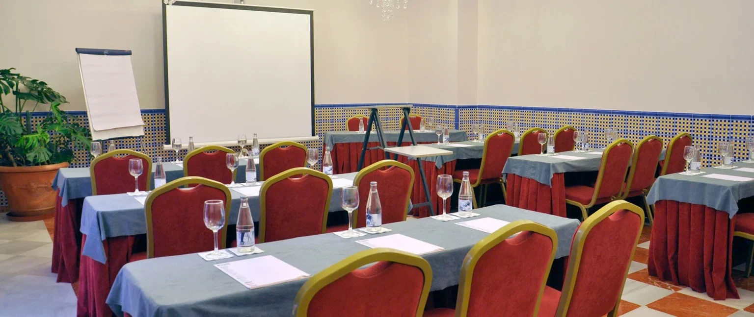Sala de eventos con mesas, sillas rojas y pantalla de proyecci&oacute;n.