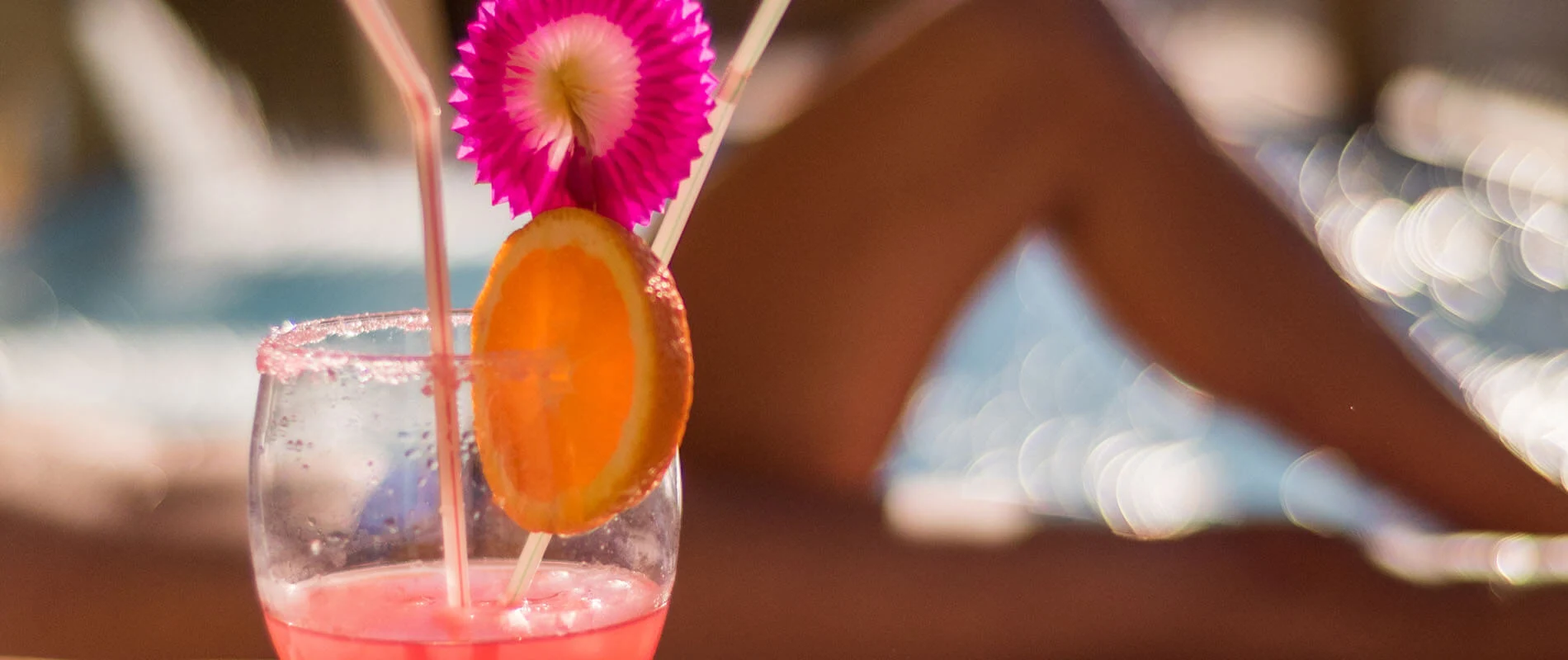 Bebida con hielo en vaso, rodaja de naranja y adorno fucsia en el popote
