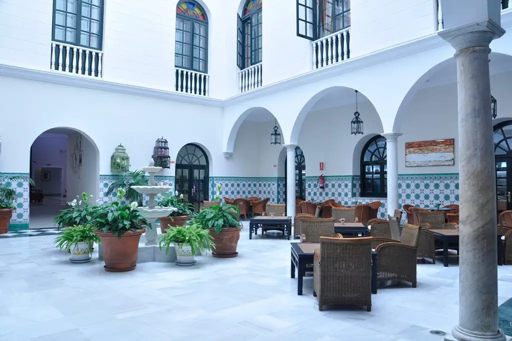 Patio andaluz blanco con arcos, macetas y mobiliario bajo faroles