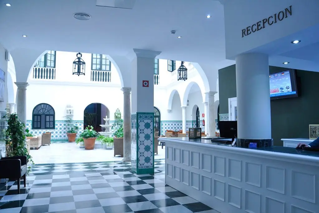 Recepci&oacute;n en hotel con patio interior blanco y azulejos, mostrador blanco