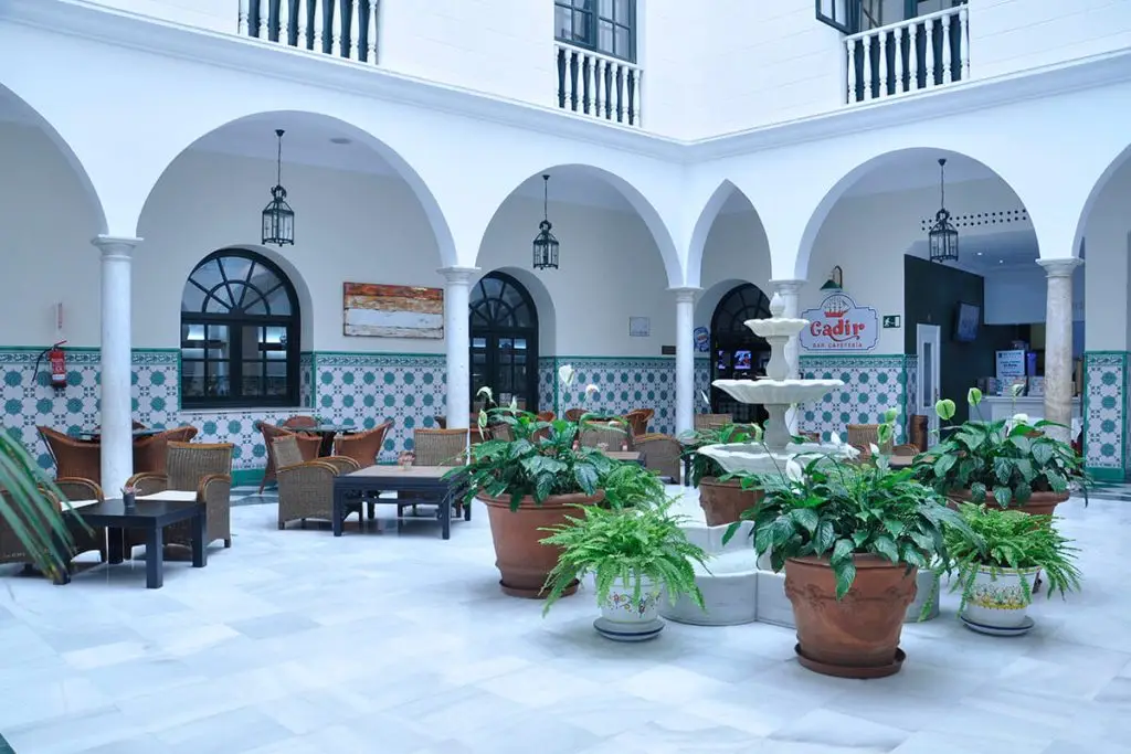 Patio andaluz con arcos blancos, macetas de plantas y mesas al aire libre