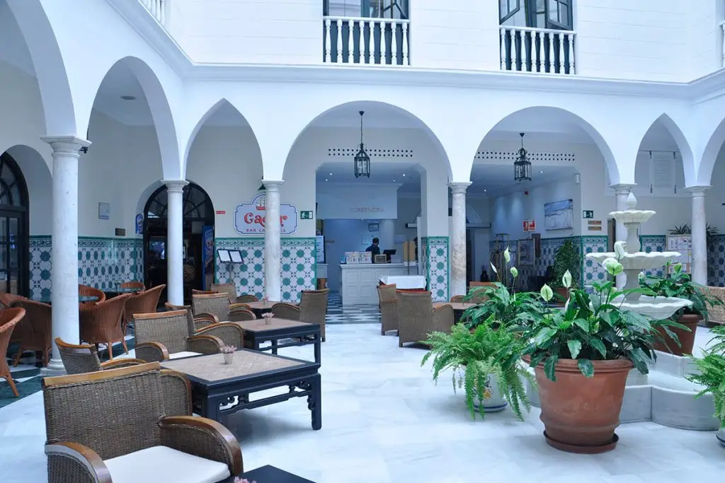 Patio interior blanco con arcos, mesas y plantas en macetas.