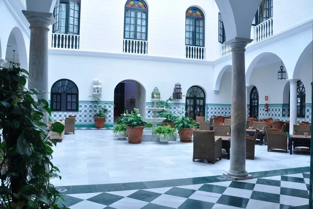 Patio andaluz con azulejos, columnas y mesas bajo balcones y arcos blancos