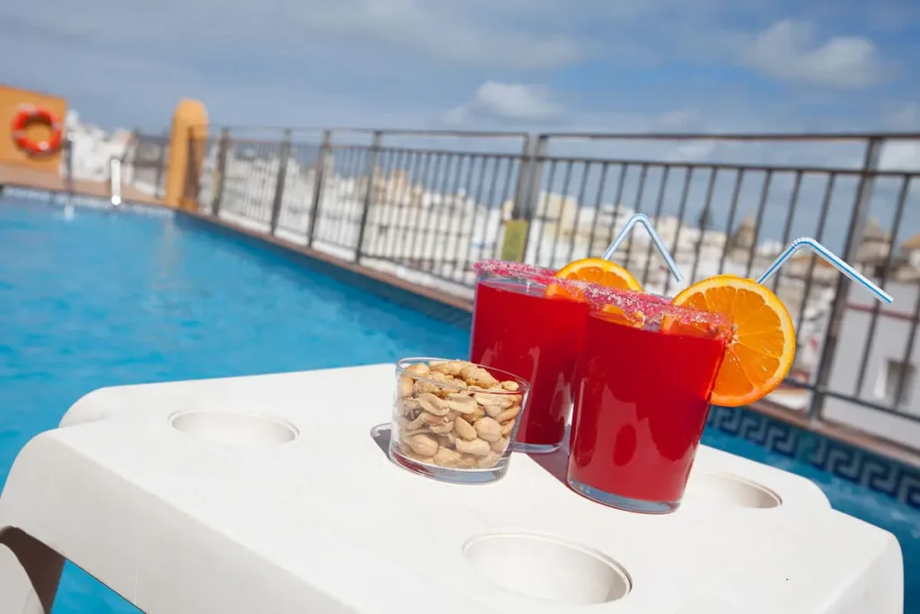 Cocteles rojos con rodajas de naranja y piscina al fondo