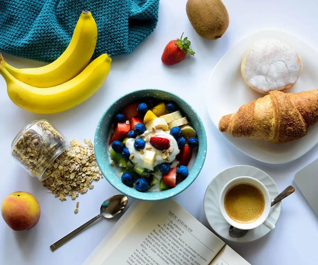 Desayuno saludable: bowl con frutas y granola, caf&eacute;, pl&aacute;tanos, kiwis y panecillo