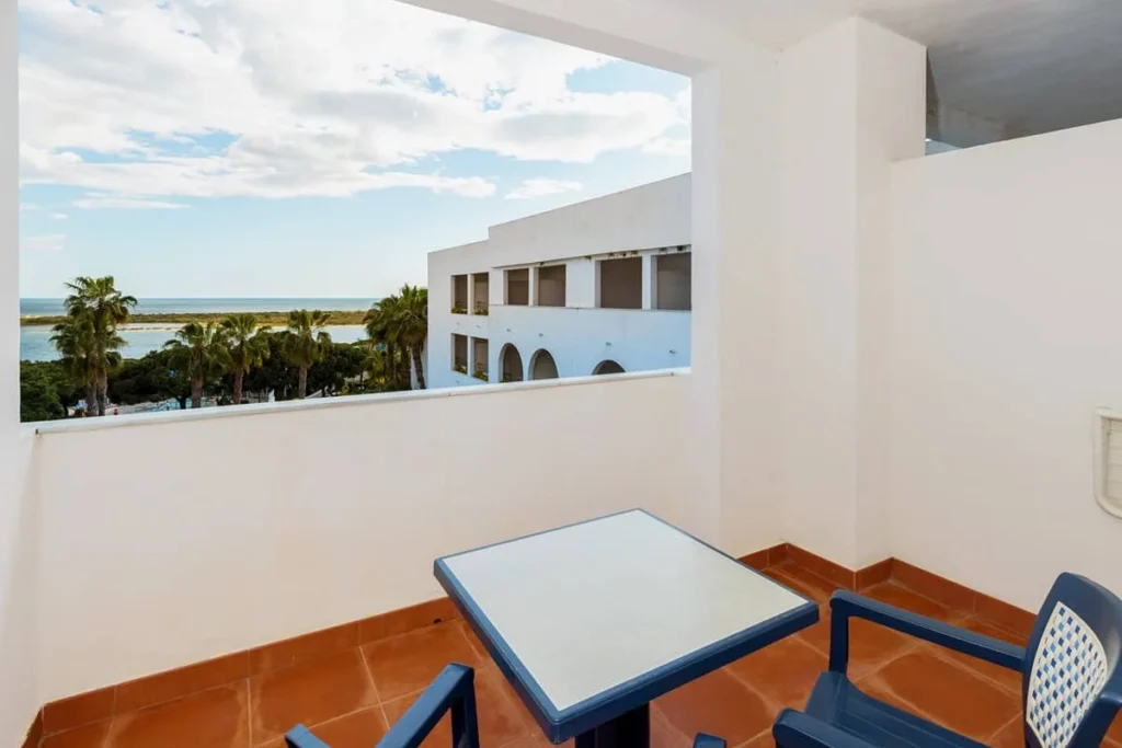 Terraza con mesa azul y vista al mar y palmeras desde un edificio blanco