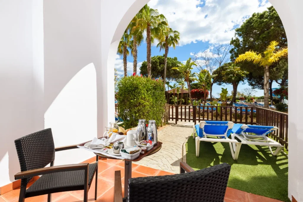 Terraza con mesa y sillas, c&eacute;sped y palmeras junto a alberca al aire libre