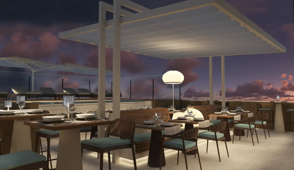 Terraza con mesas y sillas, bar iluminado y vista al atardecer nocturno