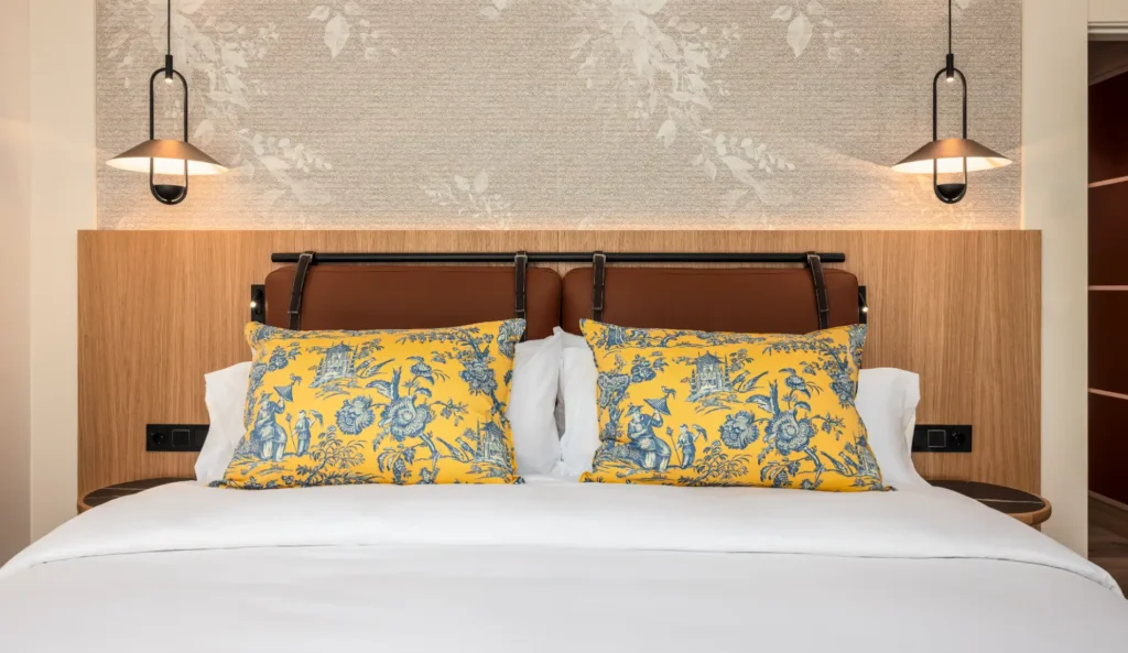 Cama doble con cojines azules y amarillos, l&aacute;mparas colgantes y pared de madera