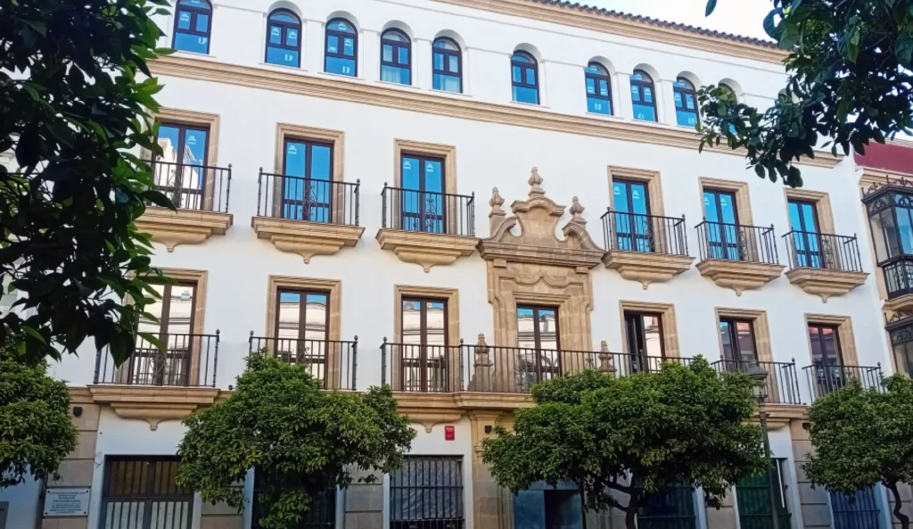 Fachada de edificio blanco con ventanas azules, balcones y balconcillos.