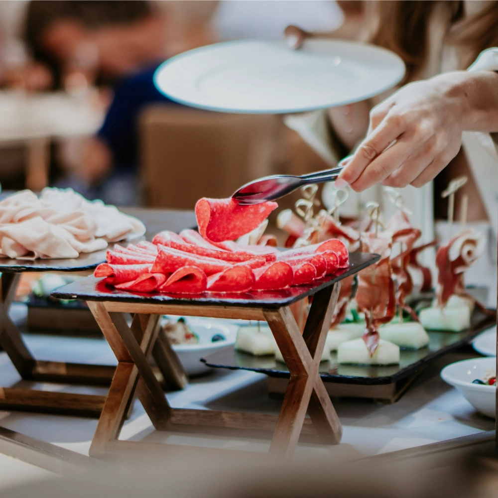 Una mano sirviendo embutidos de una mesa de aperitivos.