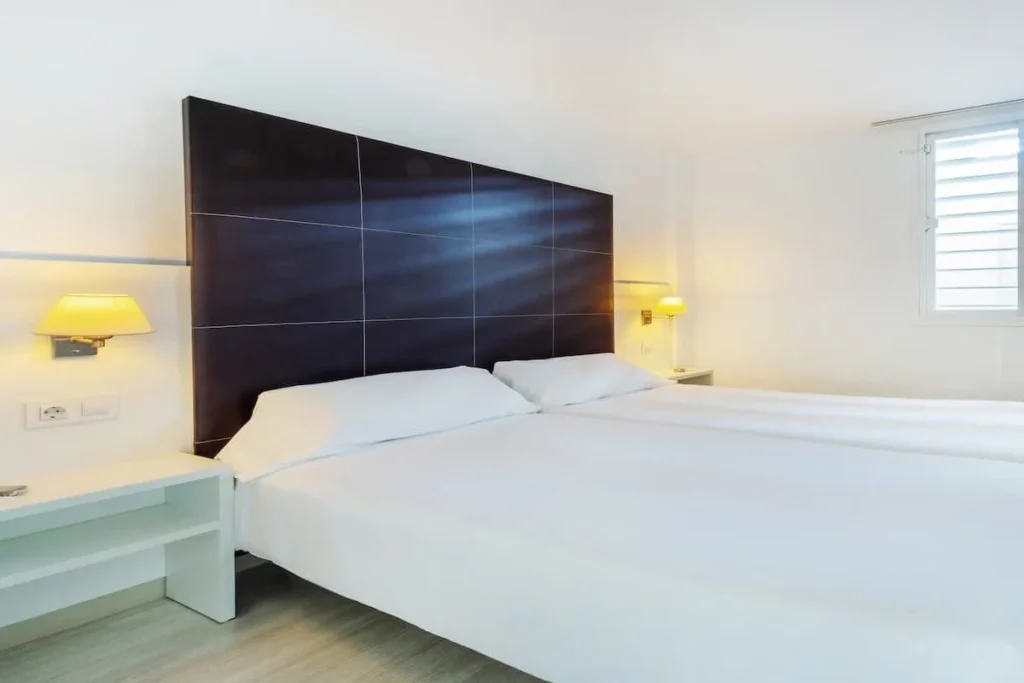 Dormitorio moderno con cama doble, cabecero oscuro y l&aacute;mparas de noche