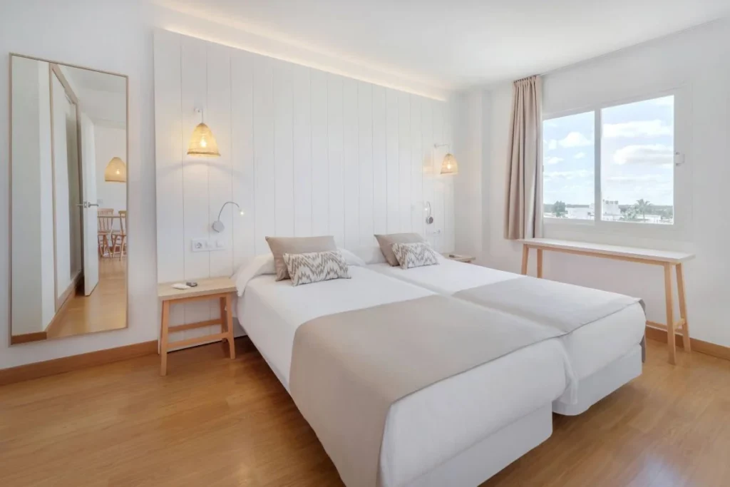 Dormitorio luminoso con dos camas, ventanal y mesita de madera