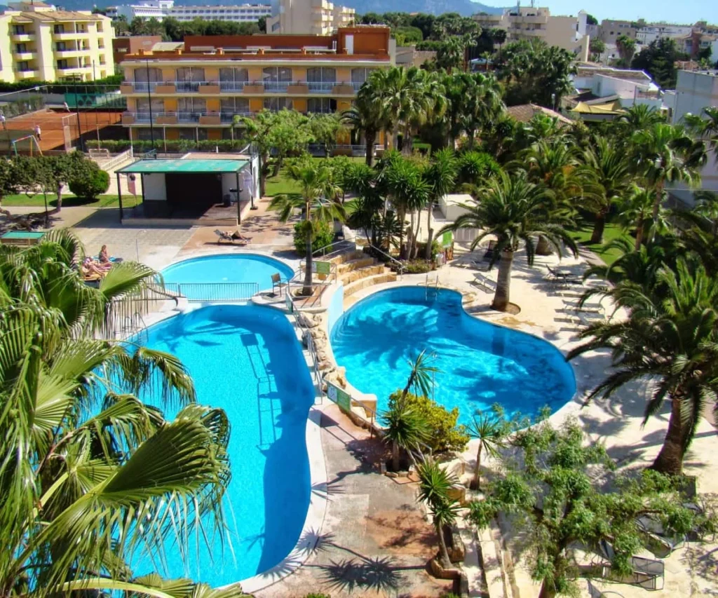Piscinas azules con palmeras y edificios en un hotel, con vistas al mar