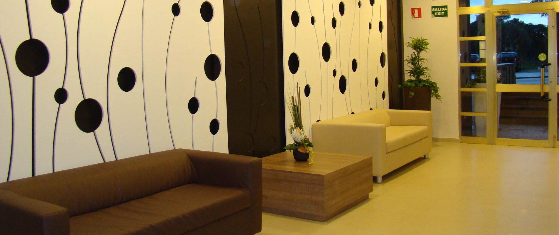 Sala moderna con sof&aacute; marr&oacute;n y amarillo, paredes decoradas y puerta de salida.