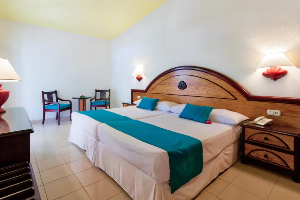 Dormitorio con cama doble, almohadas azules y l&aacute;mparas de pared.