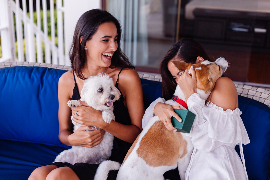 Dos chicas abrazando a sus perros sentadas en un sofá sonriendo