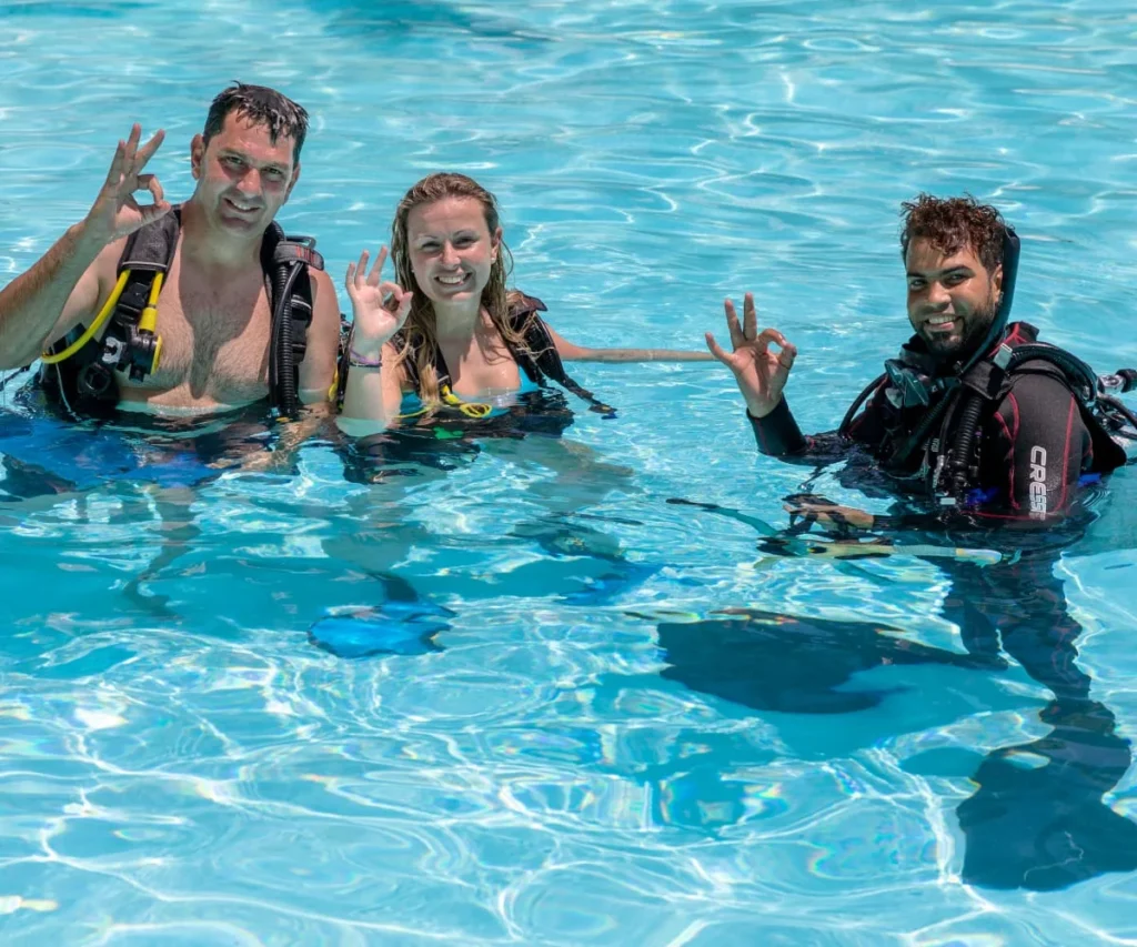 Tres buceadores sonr&iacute;en y saludan en el agua con equipo de snorkel.