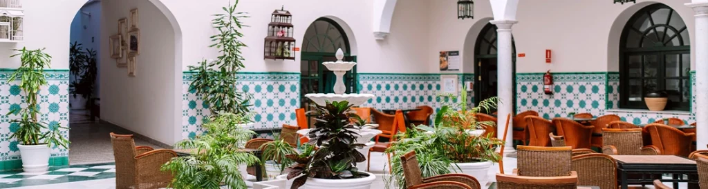 Patio interior con fuente, plantas y sillas, decorado con azulejos geom&eacute;tricos.