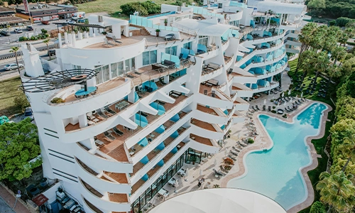 Edificio moderno con balcones y piscina curva en entorno verde.