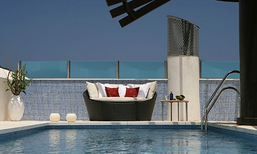 Piscina con cama exterior y cojines rojos en un ambiente moderno.