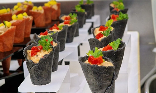 Conos gourmet negros con hierbas y pimientos en platos de presentaci&oacute;n.