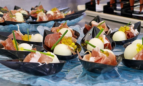Bocaditos gourmet con prosciutto y bolitas en platos de presentaci&oacute;n elegante.