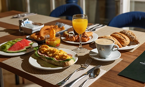 Desayuno en una mesa con caf&eacute;, jugo, pan, fruta y huevos revueltos.