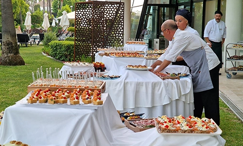 Chefs preparando una mesa de aperitivos al aire libre en un jard&iacute;n elegante.