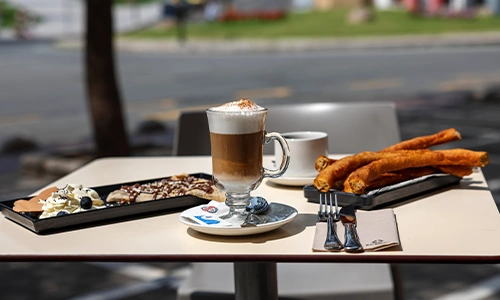 Mesa con caf&eacute;, churros y postres al aire libre.