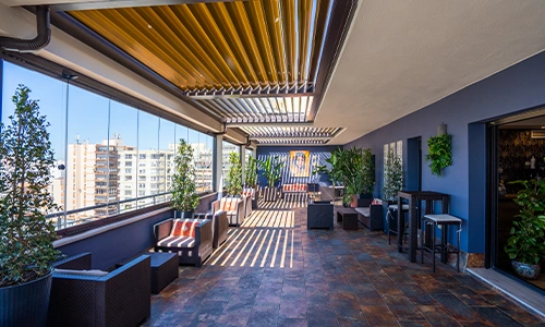 Terraza moderna con muebles y plantas, techada por p&eacute;rgola de lamas.