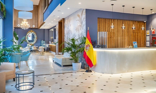 Lobby moderno con recepci&oacute;n, bandera de Espa&ntilde;a y decoraci&oacute;n elegante.