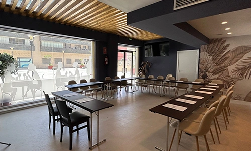 Sala de reuniones moderna con mesas en U y ventanales grandes.