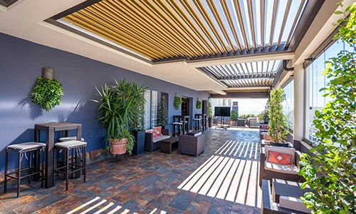 Terraza con plantas, techo de lamas y muebles exteriores en un espacio amplio.