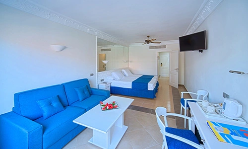 Habitaci&oacute;n de hotel luminosa con sof&aacute; azul, cama doble y escritorio.