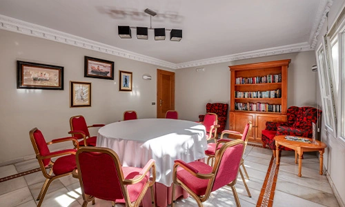 Sala de reuniones con mesa redonda, sillas rojas y librero de madera.
