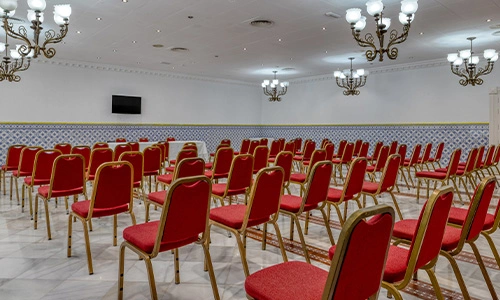Sala de conferencias con sillas rojas y l&aacute;mparas de ara&ntilde;a.
