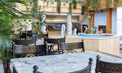 &Aacute;rea de comedor elegante con plantas y fuente decorativa en el fondo.