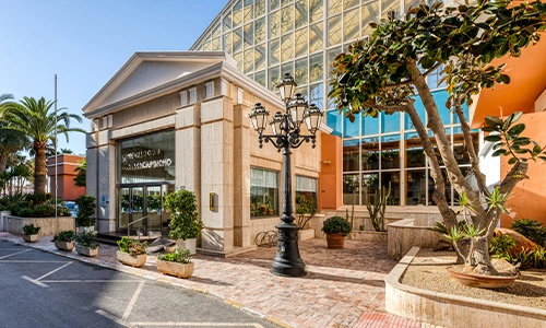 Entrada de un edificio moderno con vidrieras y plantas en el exterior.