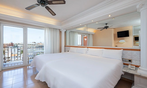 Habitaci&oacute;n de hotel moderna con cama grande, espejo y terraza con vista a la ciudad.