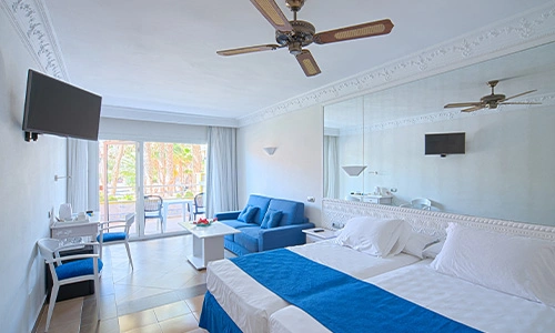 Habitaci&oacute;n de hotel luminosa con cama doble, sof&aacute; y balc&oacute;n.