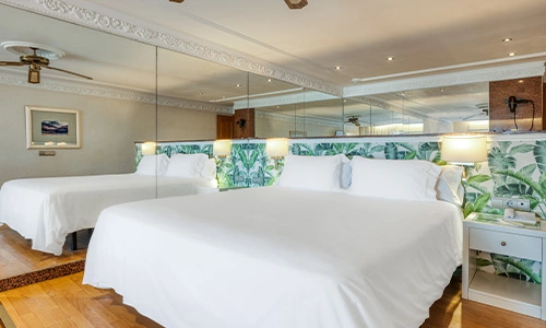 Habitaci&oacute;n de hotel con dos camas, espejos y decoraci&oacute;n de hojas verdes.