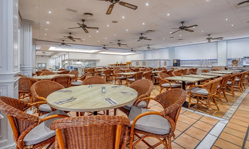 Comedor amplio con sillas y mesas de mimbre en un restaurante vac&iacute;o.