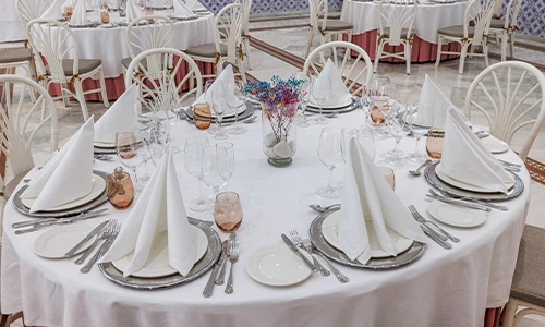 Mesa redonda elegantemente decorada con cubiertos y copas en un sal&oacute;n de eventos.