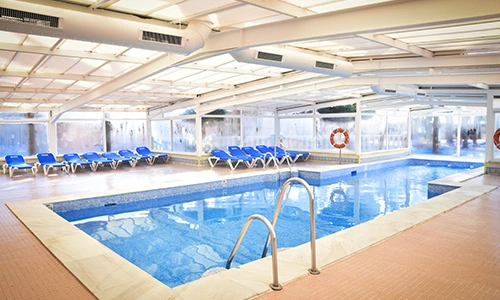 Piscina interior con sillas azules alineadas al fondo y techado transparente.