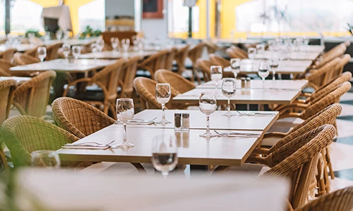 Restaurante vac&iacute;o con mesas puestas y sillas de mimbre.