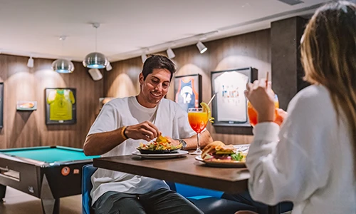 Personas comiendo en un restaurante con mesa de billar y decoraciones deportivas.