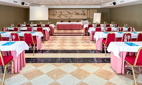 Sala de conferencias elegante con mesas y sillas rojas alineadas.